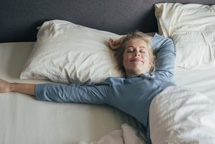 Eine lächelnde Frau streckt im Bett die Arme aus
